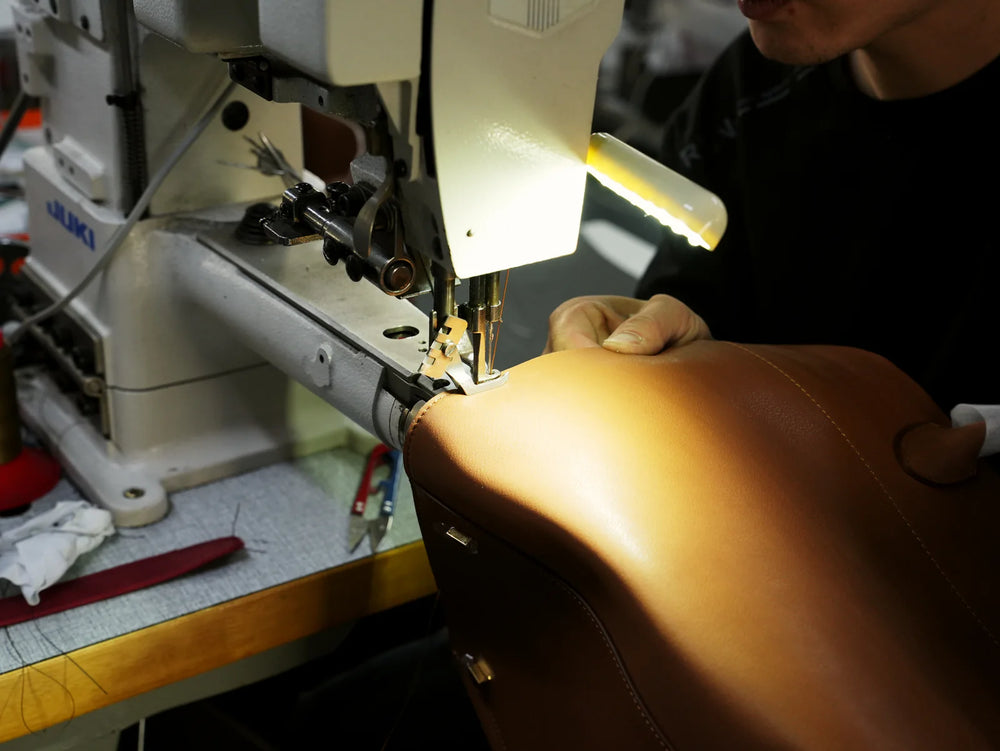 Worker stitching a brown handbag with a sewing machine in the workshop.