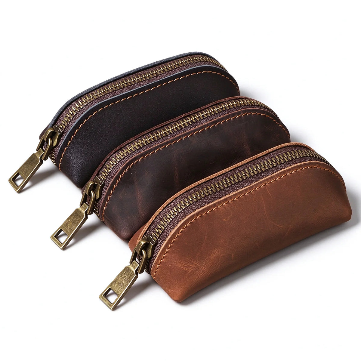 Three leather key pouches in brown, dark brown and black with matching curved zip openings.