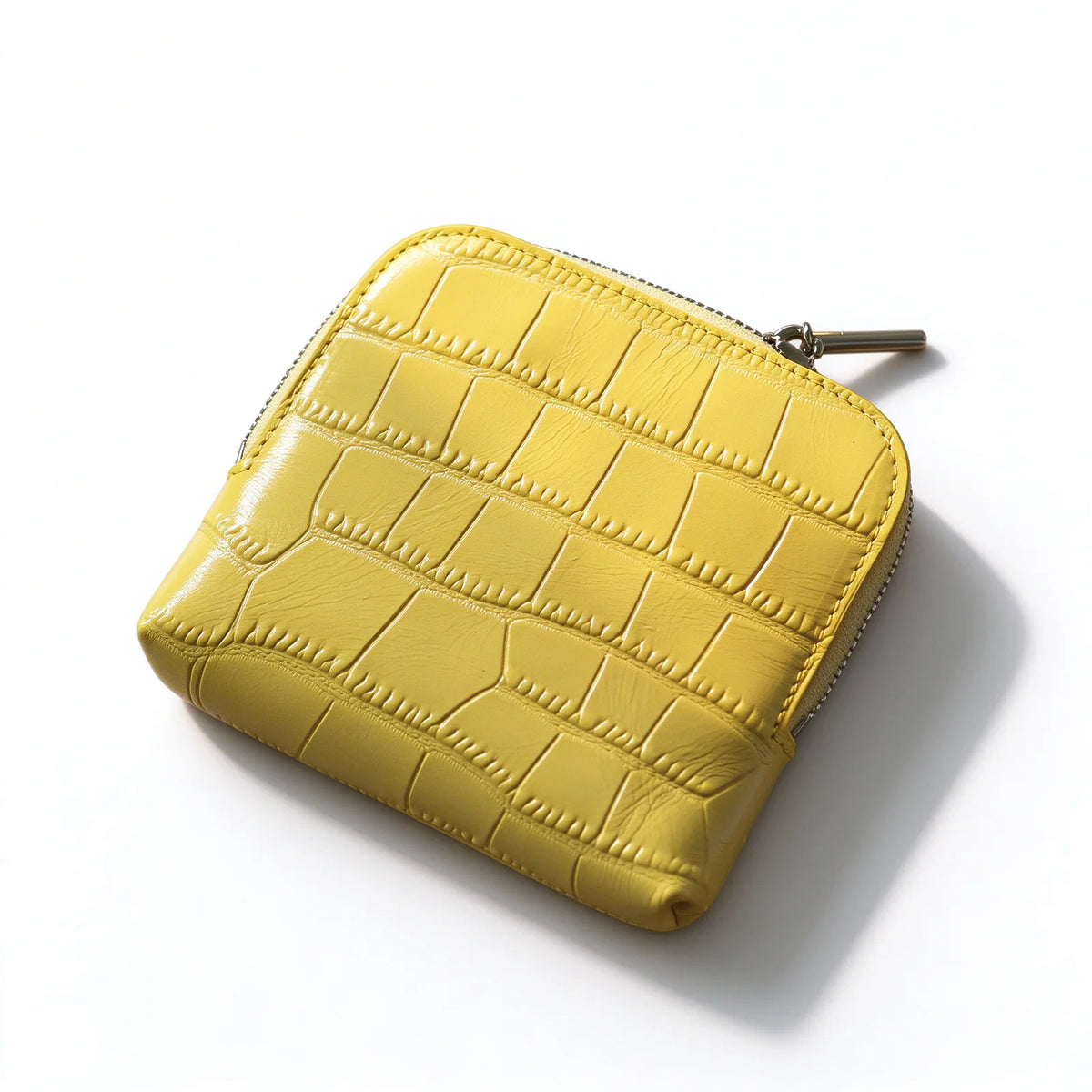Yellow crocodile-textured leather jewelry pouch with rounded corners and a silver-tone zipper, angled view.