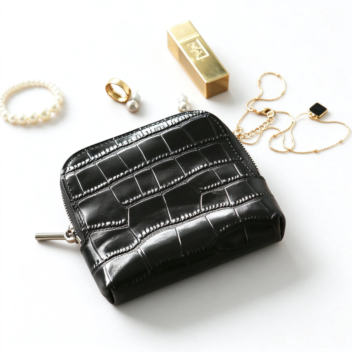 Black crocodile-textured leather jewelry pouch displayed beside necklaces, earrings and other jewelry props.