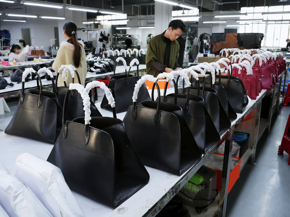 Workers beside rows of black and red top-handle handbags in the production workshop.