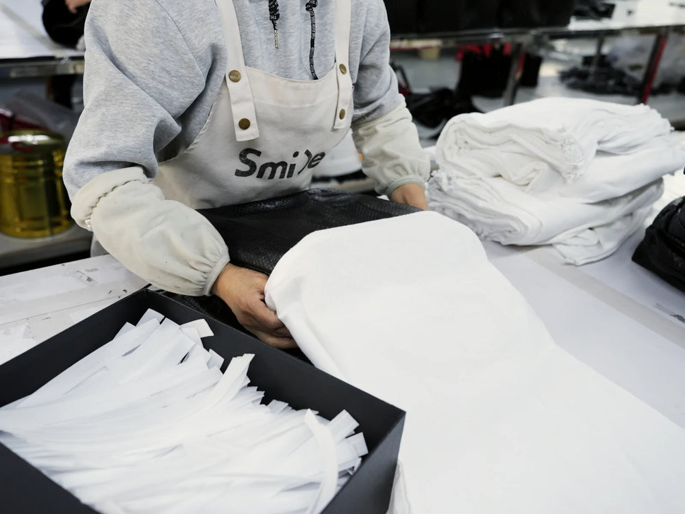 Worker covering a handbag with white protective material at a packing table.