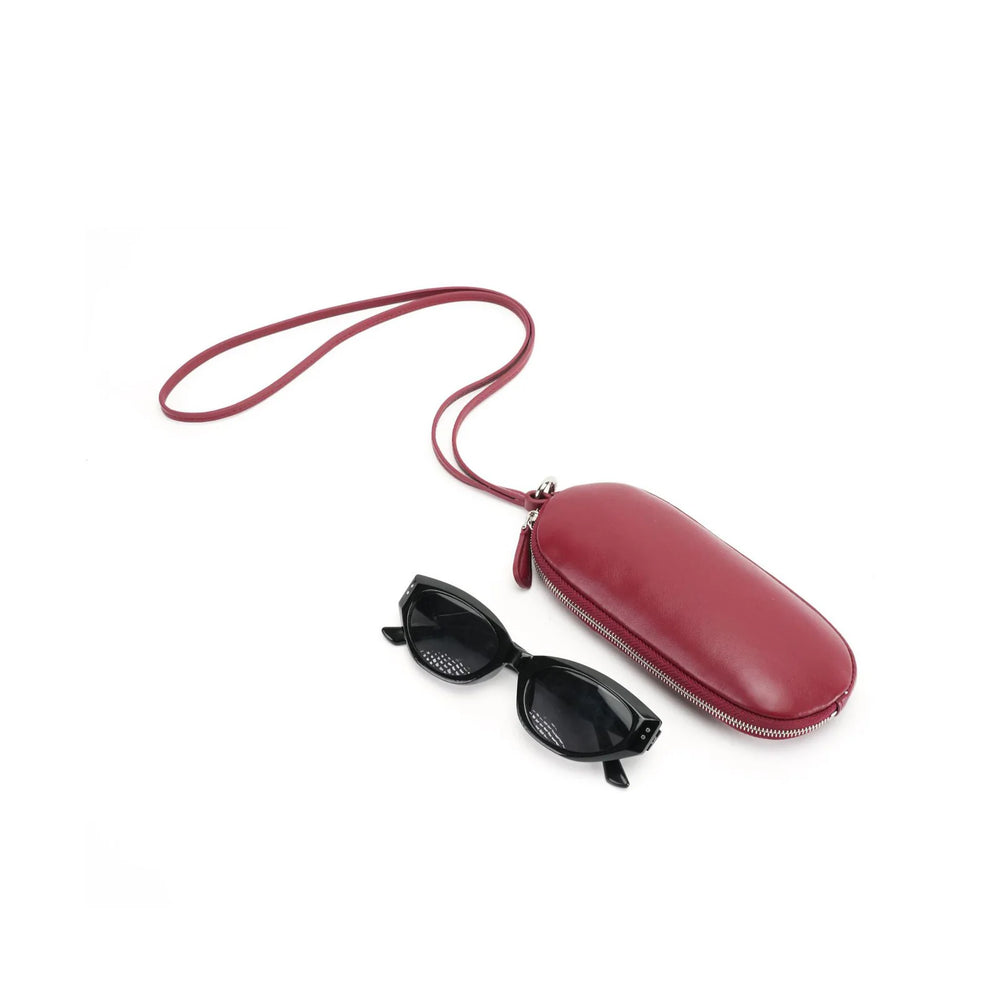 Burgundy leather eyeglass pouch with a long matching strap beside black sunglasses