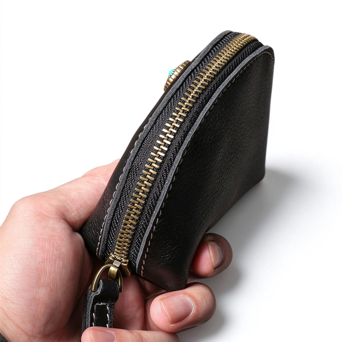 Side close-up of a black leather key pouch showing the curved metal zip and stitched edges