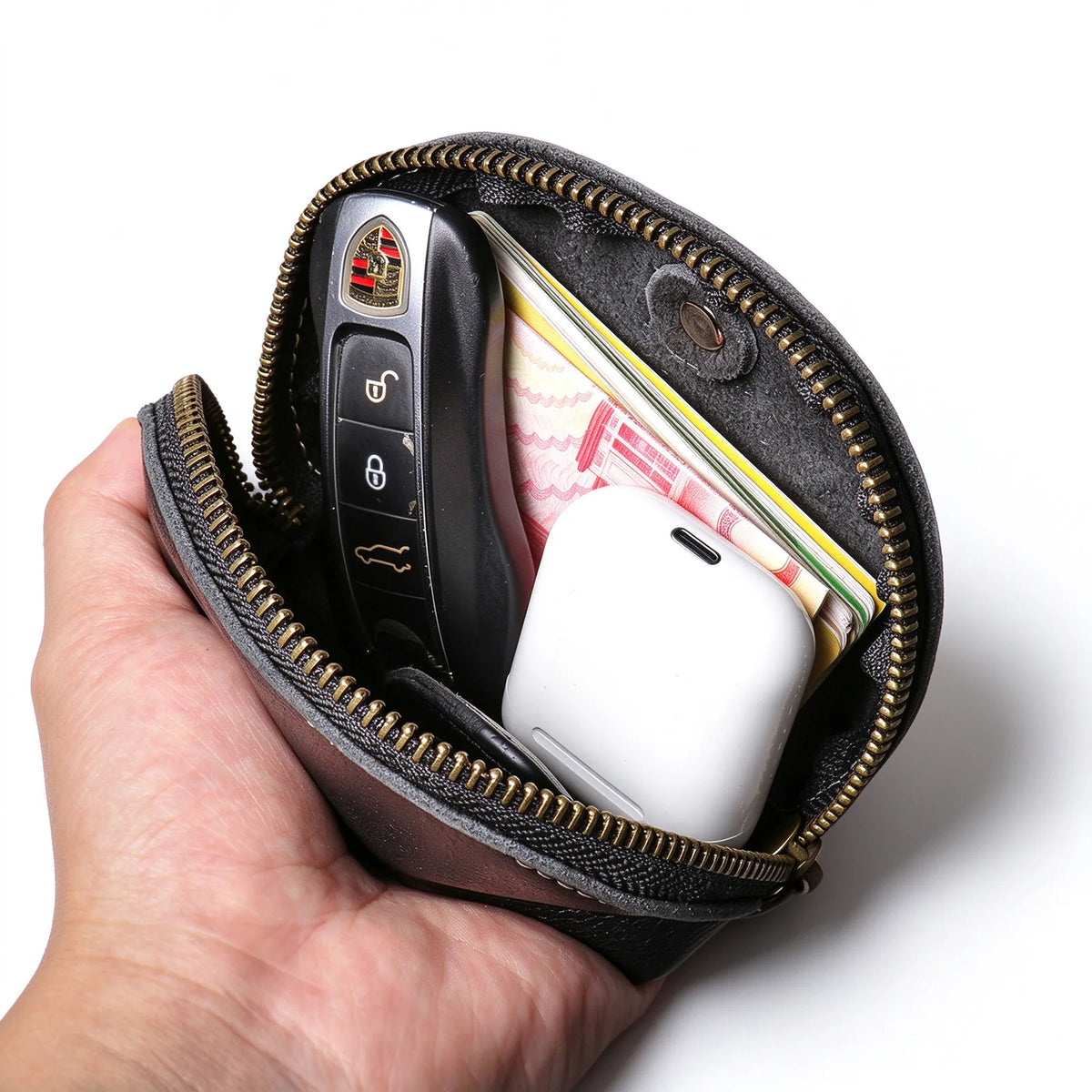 Open black leather key pouch holding a key fob, cards, banknotes and a white earbud case