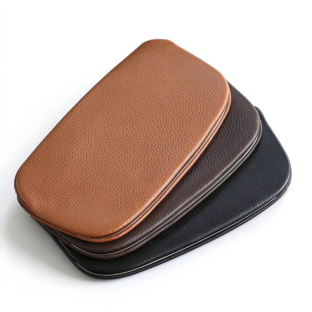 Tan, dark brown and black leather metal-frame clutch pouches stacked on a white background