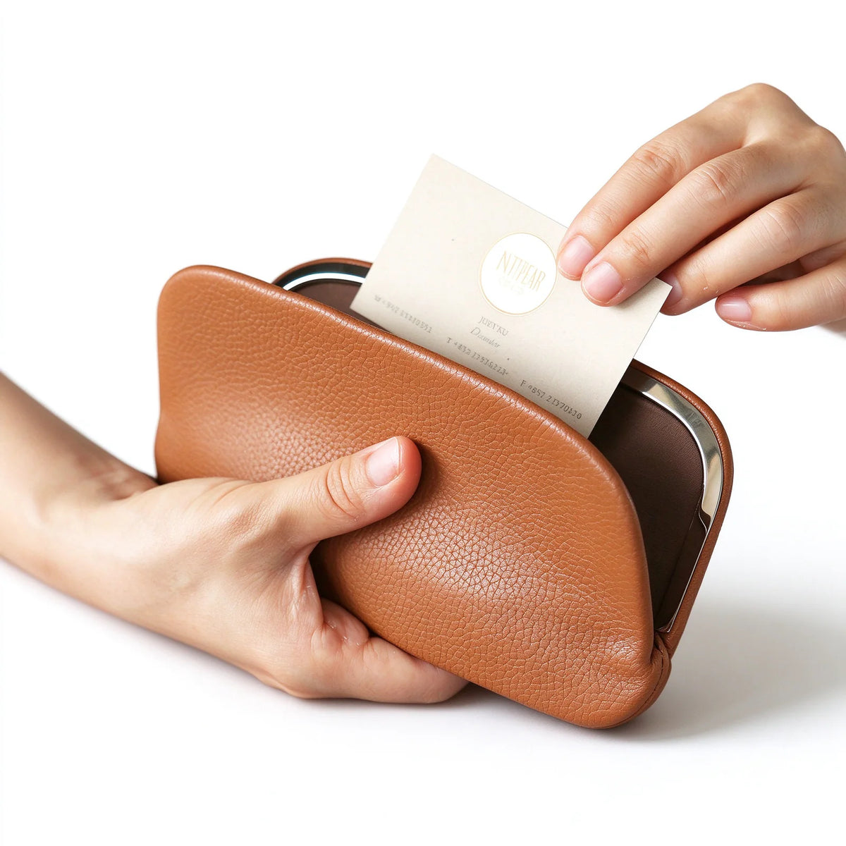 A business card being placed in an open tan leather clutch pouch with a silver-tone frame