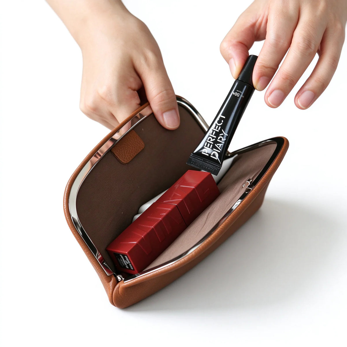 Open tan leather metal-frame clutch pouch holding cosmetics with its brown interior visible
