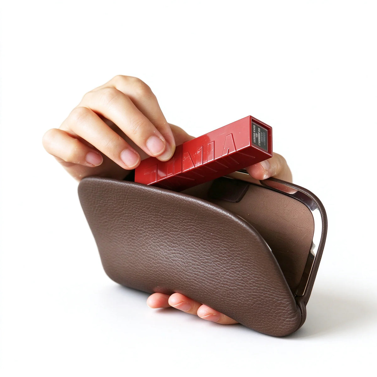 A lipstick case being placed in a dark brown leather clutch pouch with a silver-tone frame