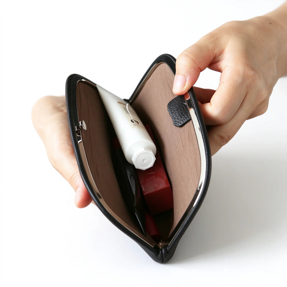 Open black leather clutch pouch holding skincare and cosmetic containers