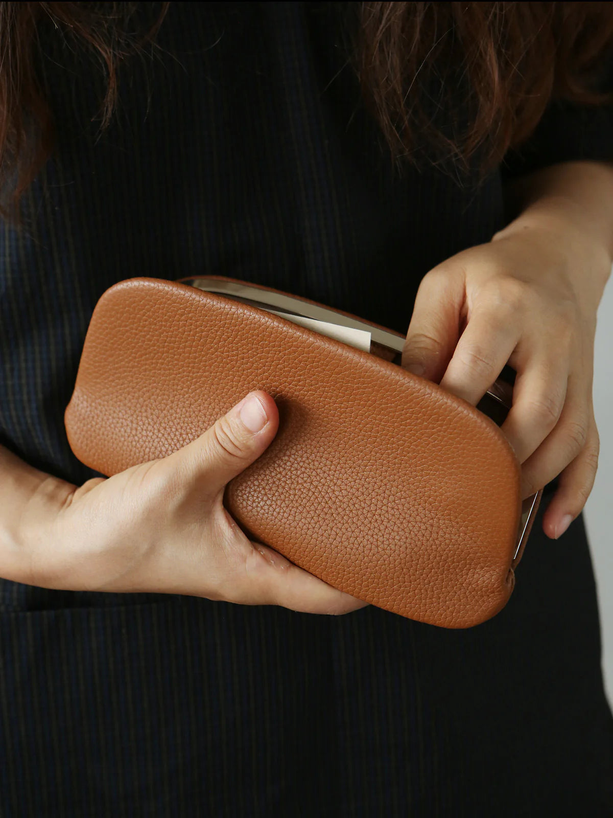Tan leather clutch pouch held in both hands with its silver-tone frame opening visible