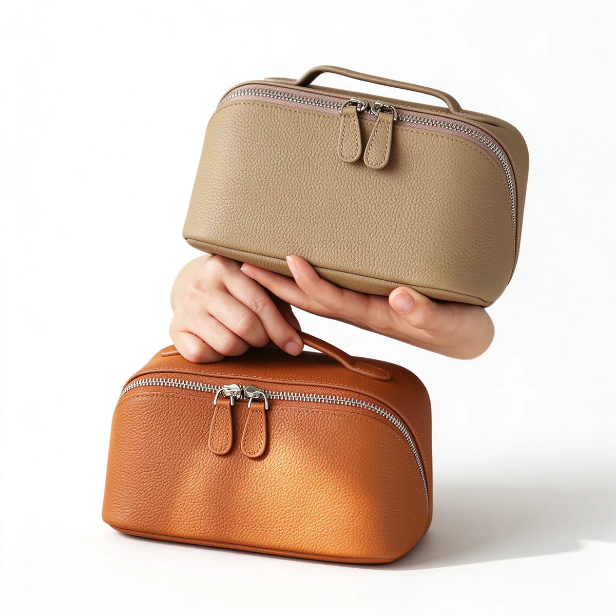 Taupe and orange leather travel makeup bags with top handles, double zip pulls and pebbled surfaces.