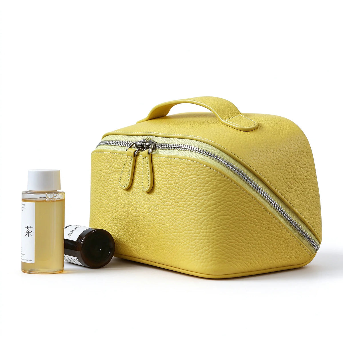Yellow leather travel makeup bag with a top handle and double zipper, shown beside small bottles.