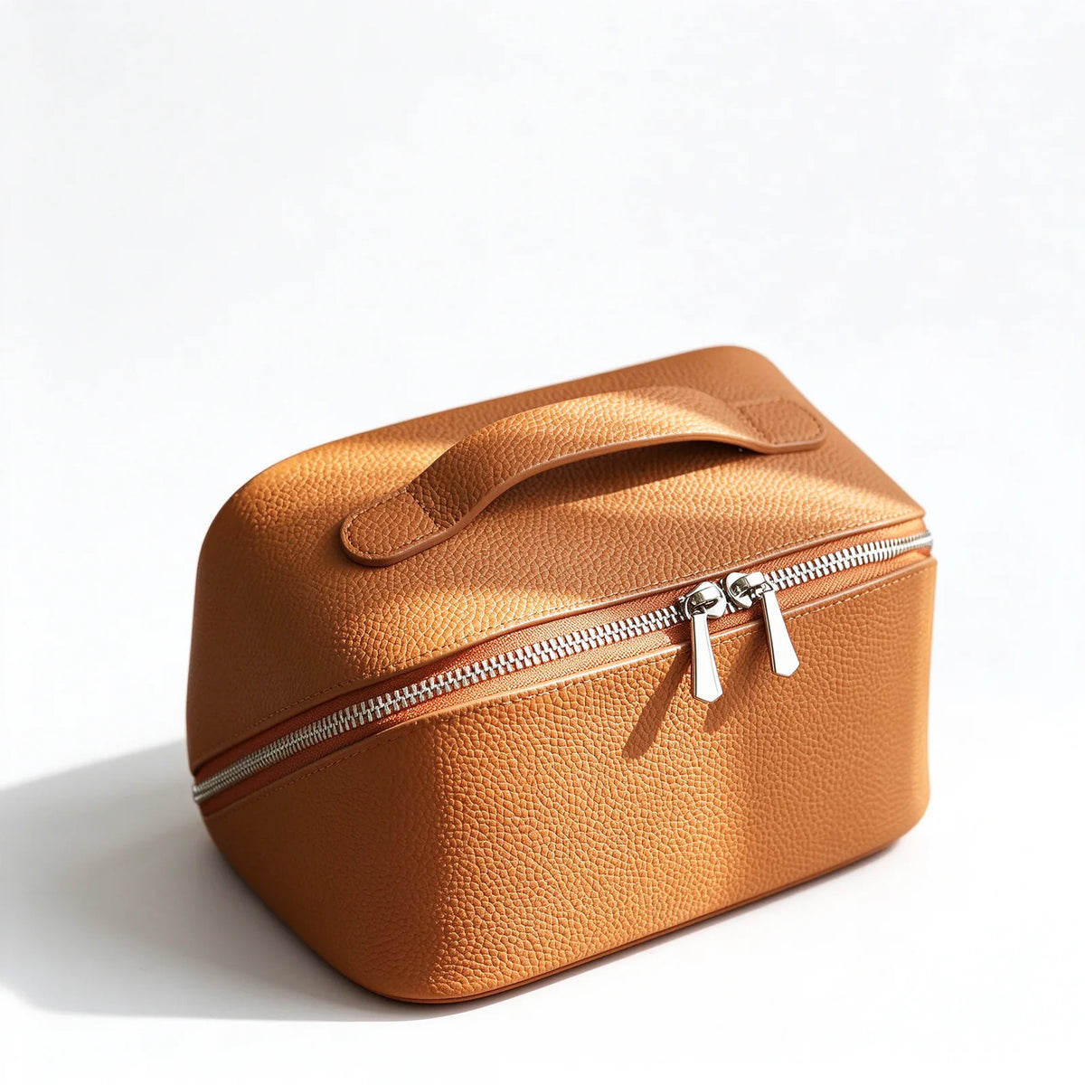 Orange leather makeup bag in an angled view showing its top handle and twin silver-tone zipper pulls.