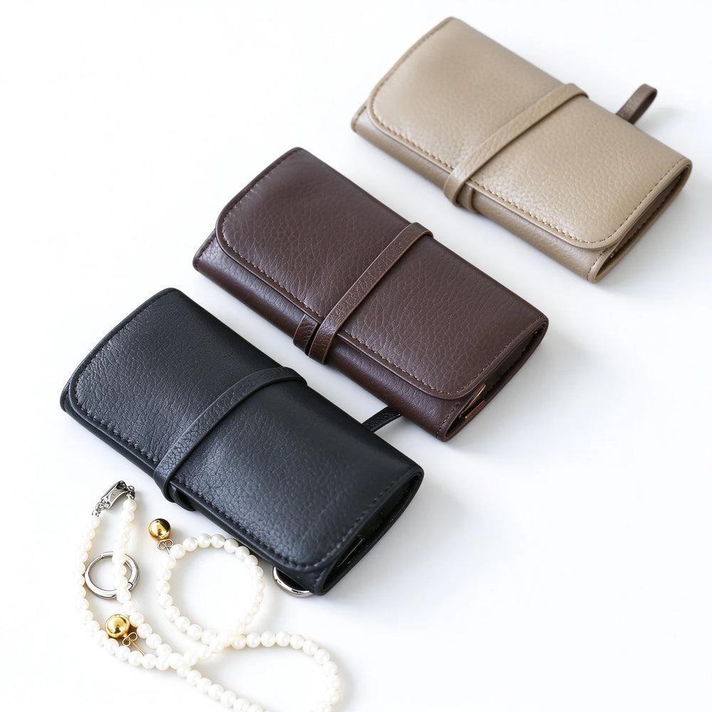 Black, dark brown and taupe leather jewelry rolls with wraparound ties beside jewelry
