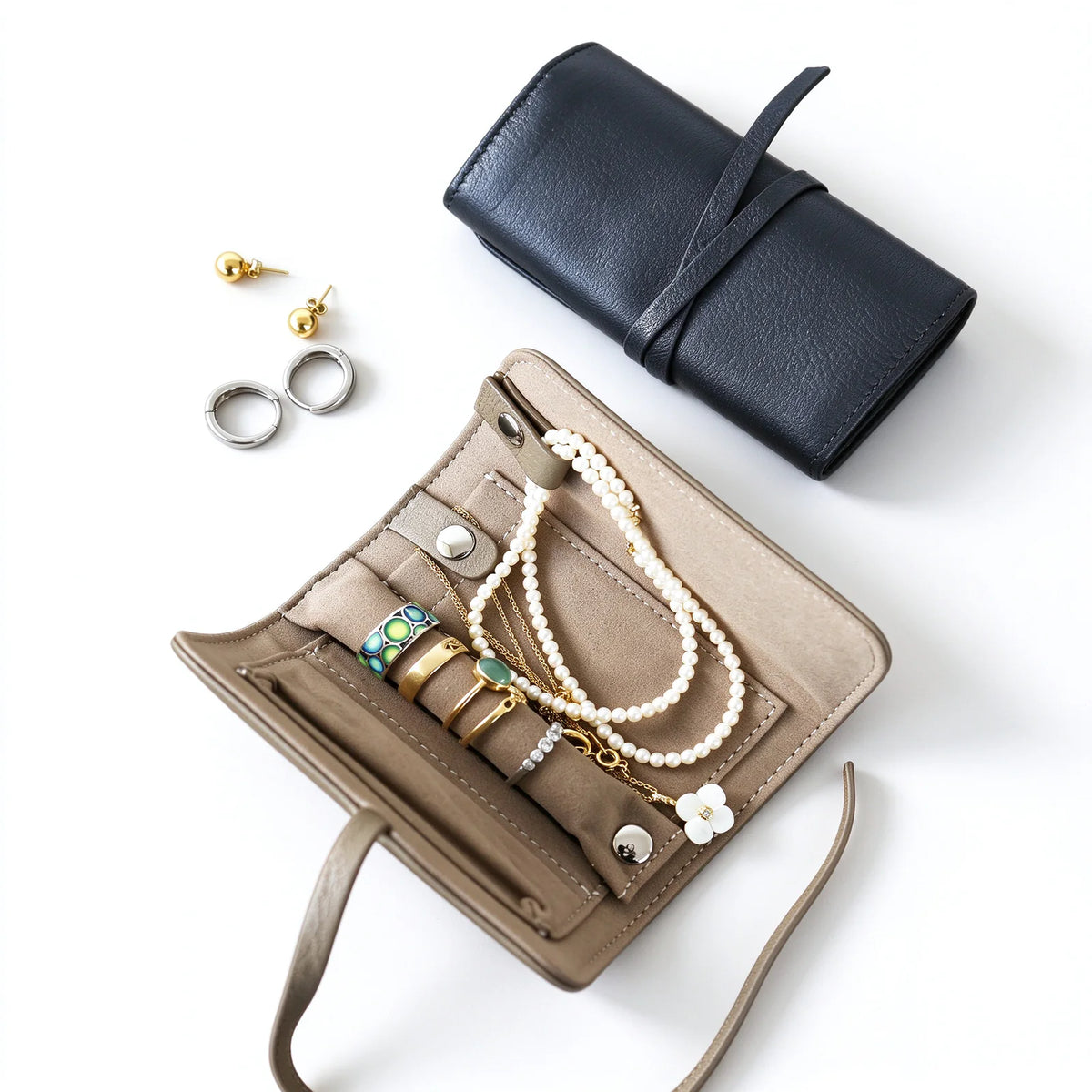 Open taupe leather jewelry roll holding rings and necklaces beside a closed black roll