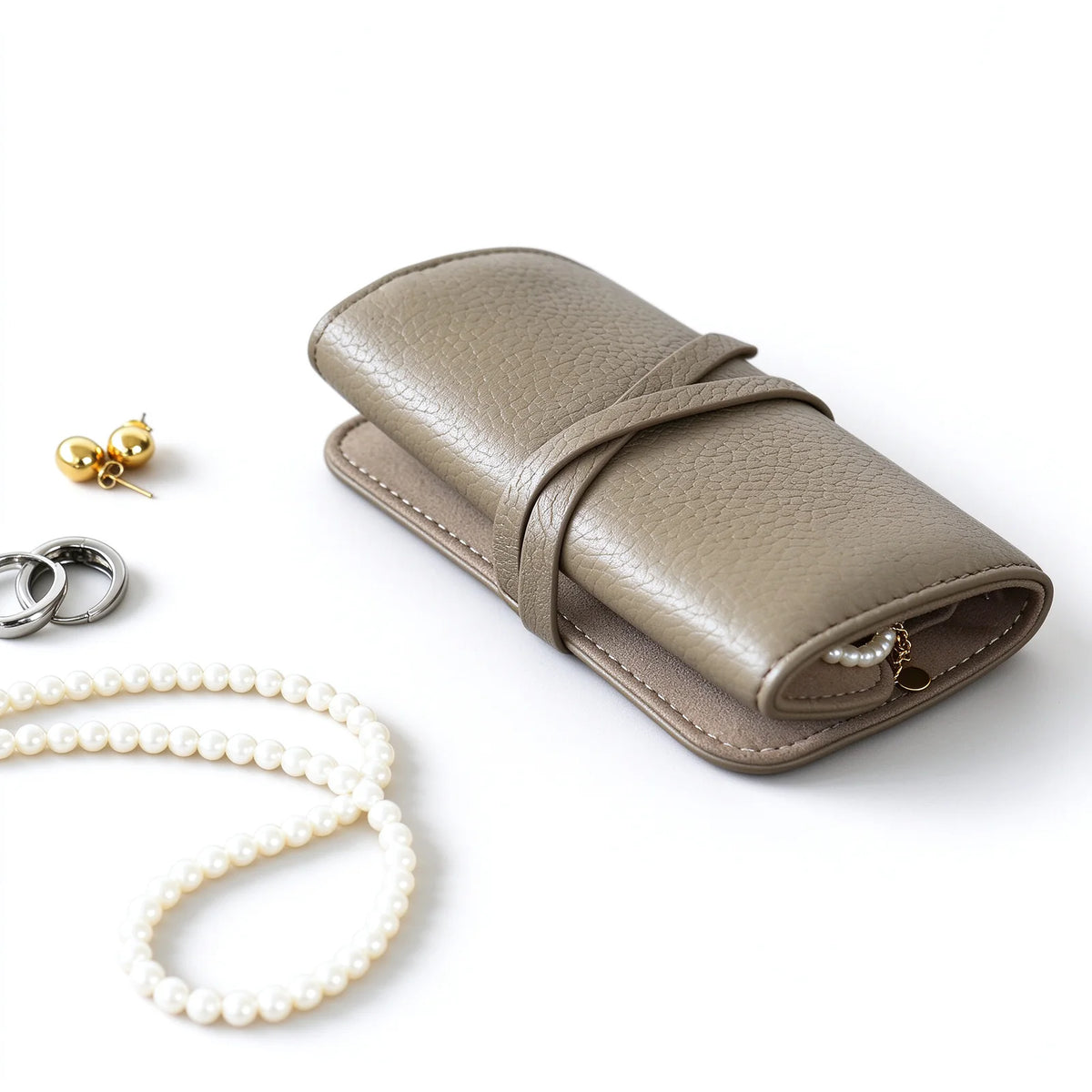 Taupe leather jewelry roll tied closed with necklaces and earrings beside it