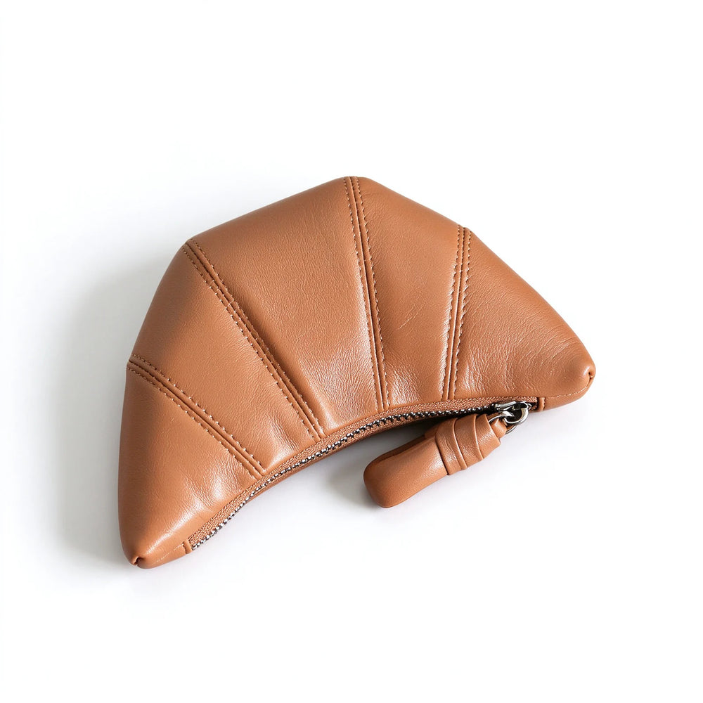 Top view of a tan crescent leather makeup pouch with stitched panels and a knotted zipper pull.