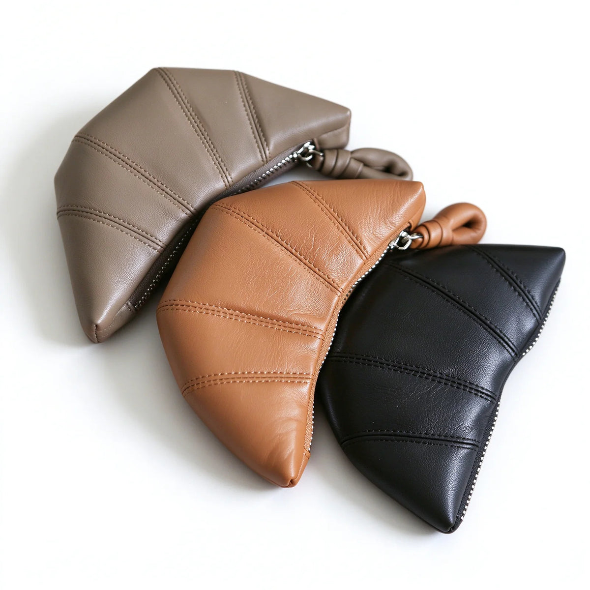 Taupe, tan and black crescent-shaped leather pouches arranged together with stitched panels and rounded zip pulls.