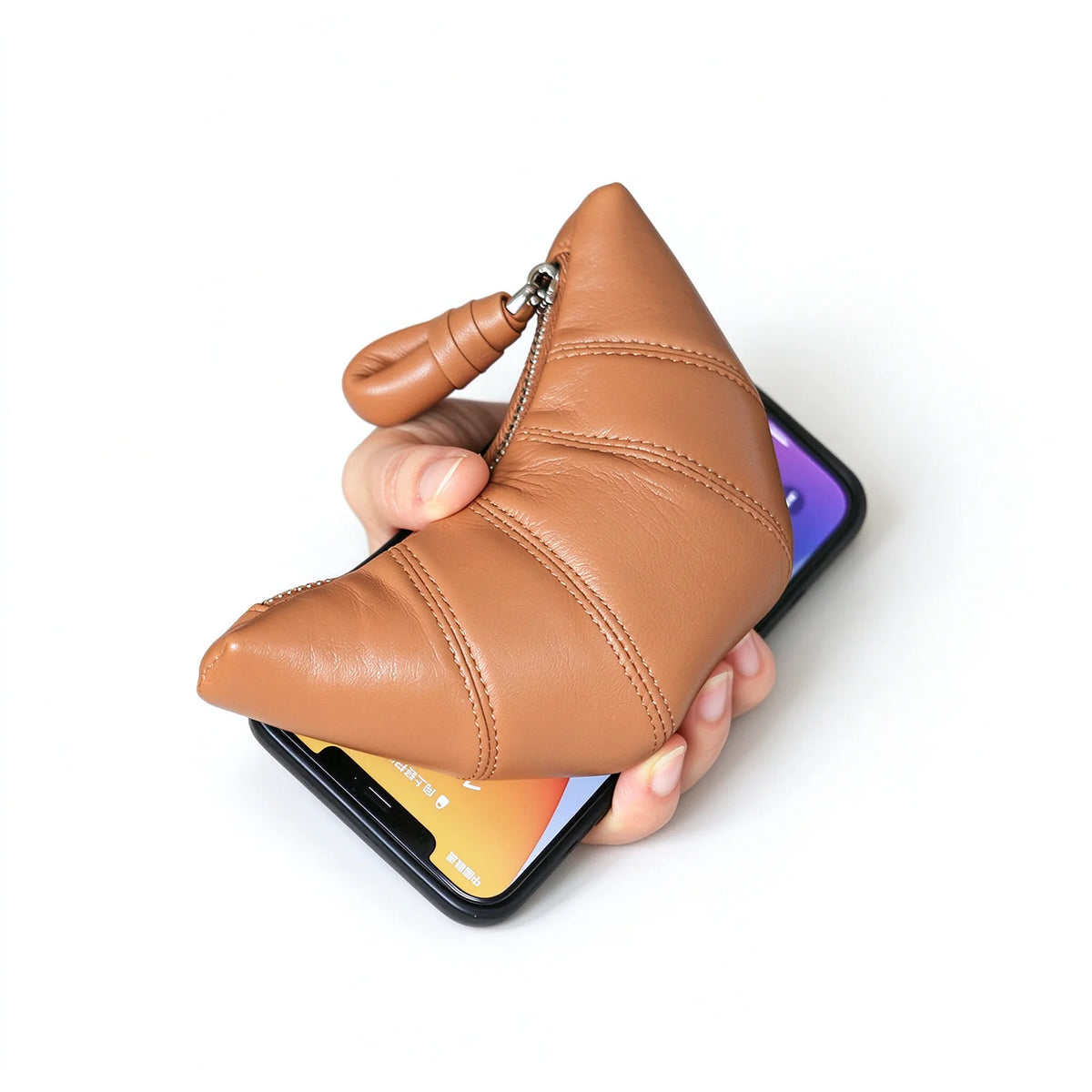 Tan crescent leather pouch held over a smartphone to show the relative size and curved stitched shape.