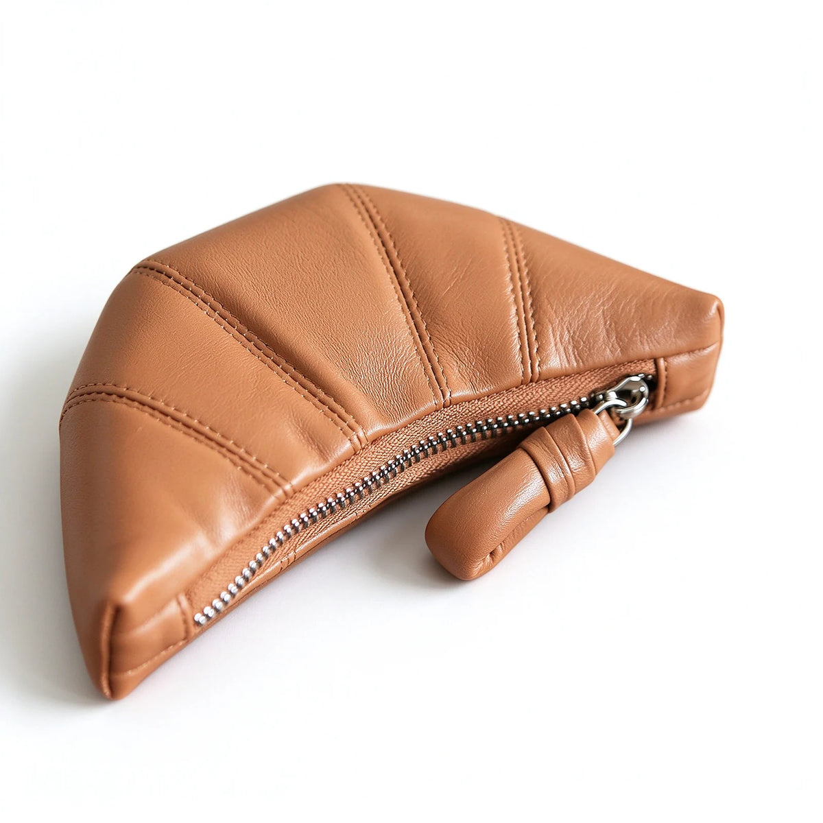 Close-up of the curved zipper, stitched leather panels and rounded knot-style pull on a tan crescent pouch.
