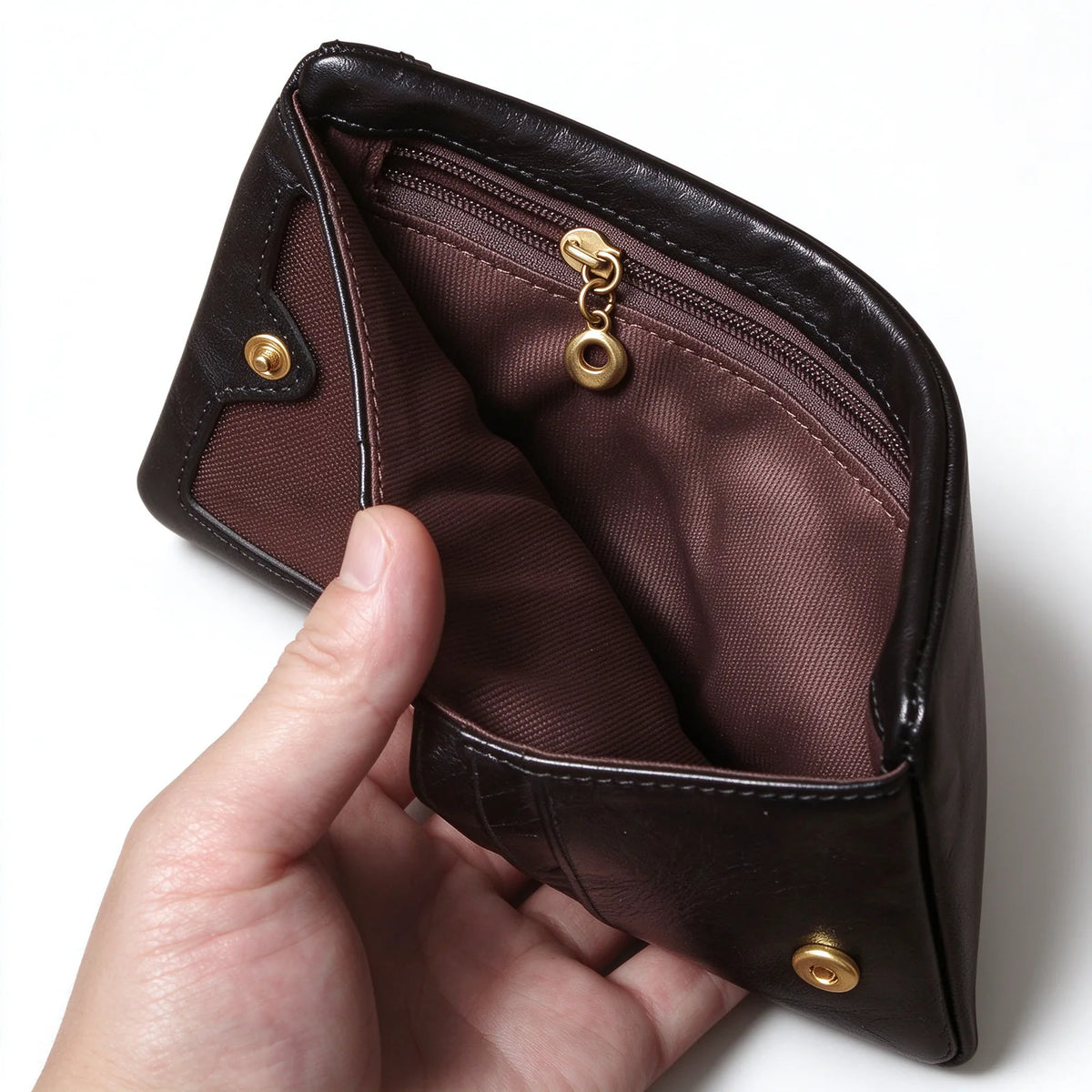 Inside detail of a black leather wallet showing brown lining and a zip pocket with a round gold-tone pull.
