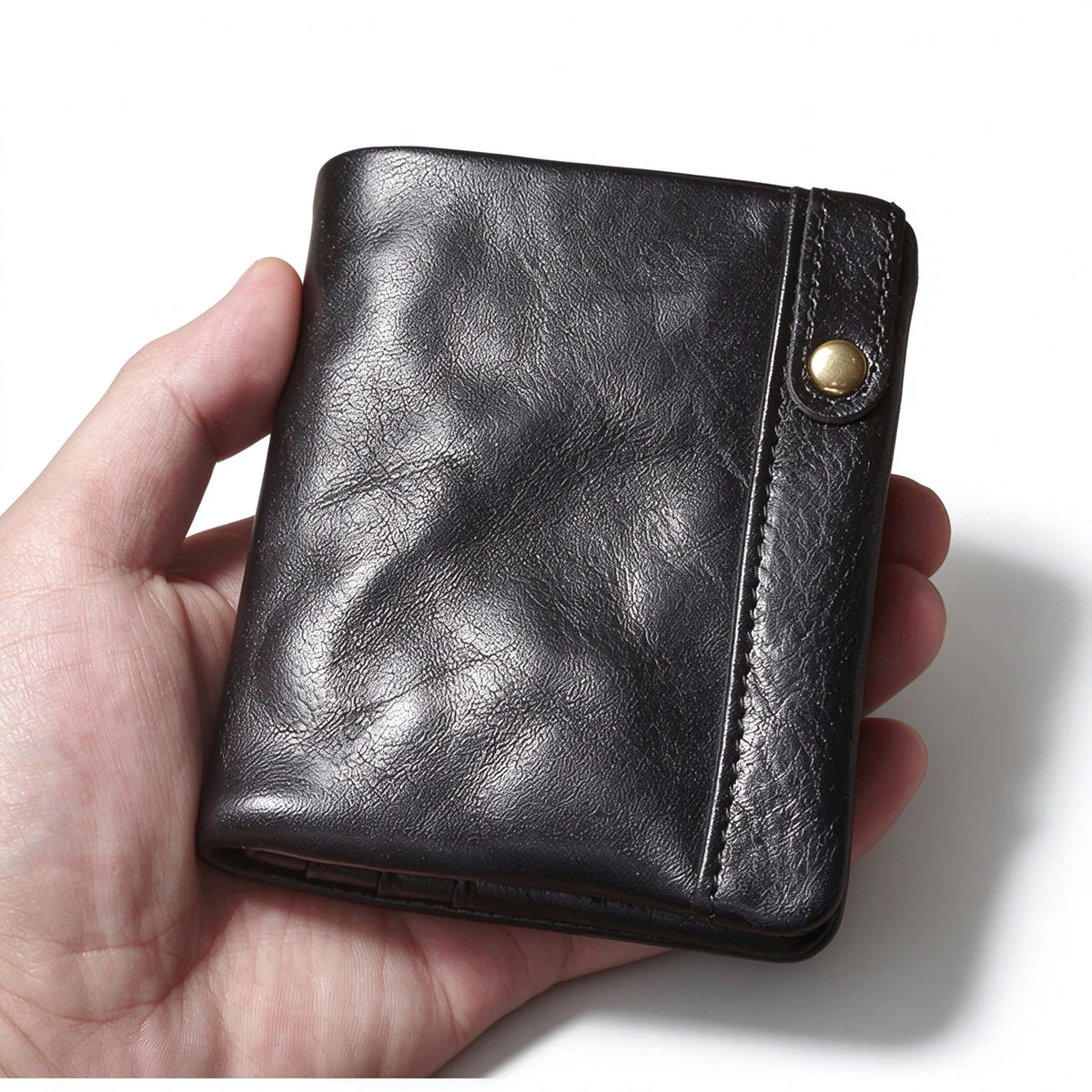 Close-up of a black leather wallet held in the palm, showing its creased surface and snap-fastened tab.