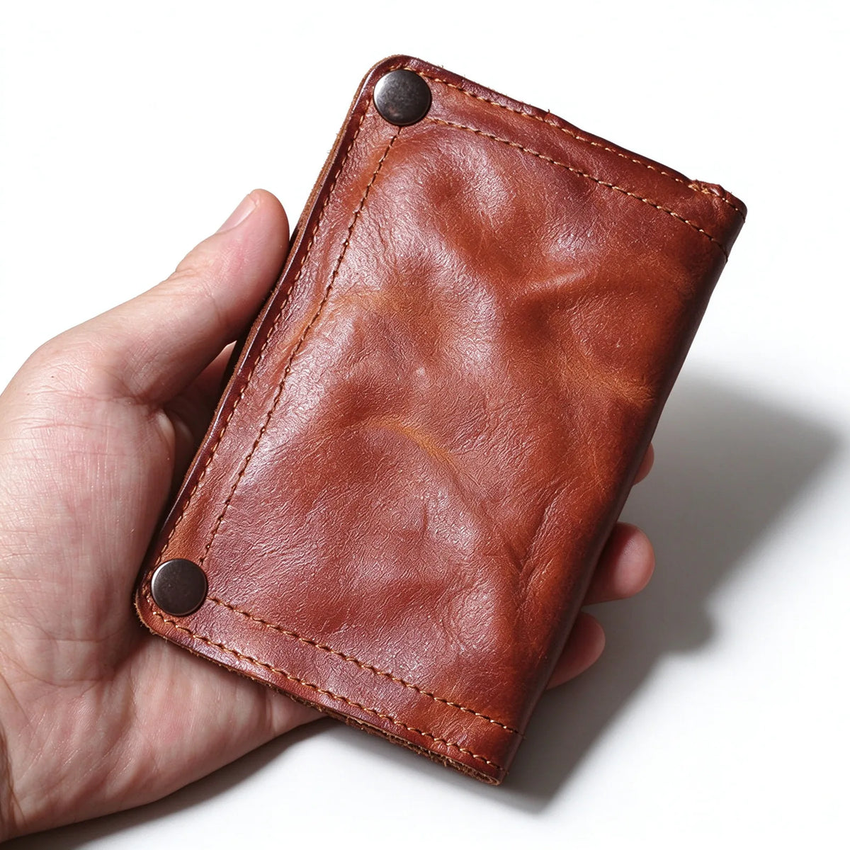 Hand-held brown leather bifold wallet showing its creased front panel, edge stitching and two snap fasteners.