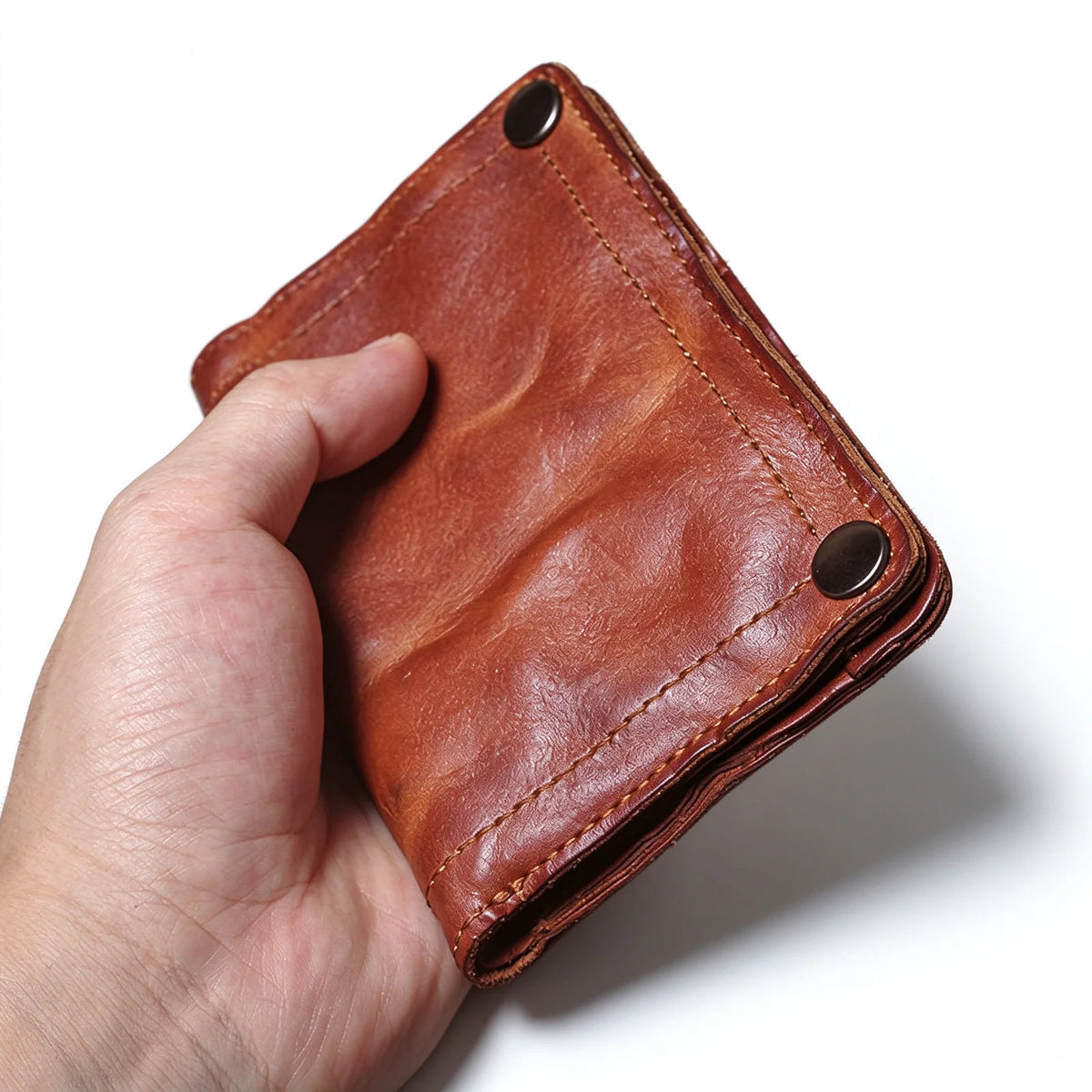 Hand-held reverse angled view of a brown leather wallet showing its folded edge and snap fasteners.