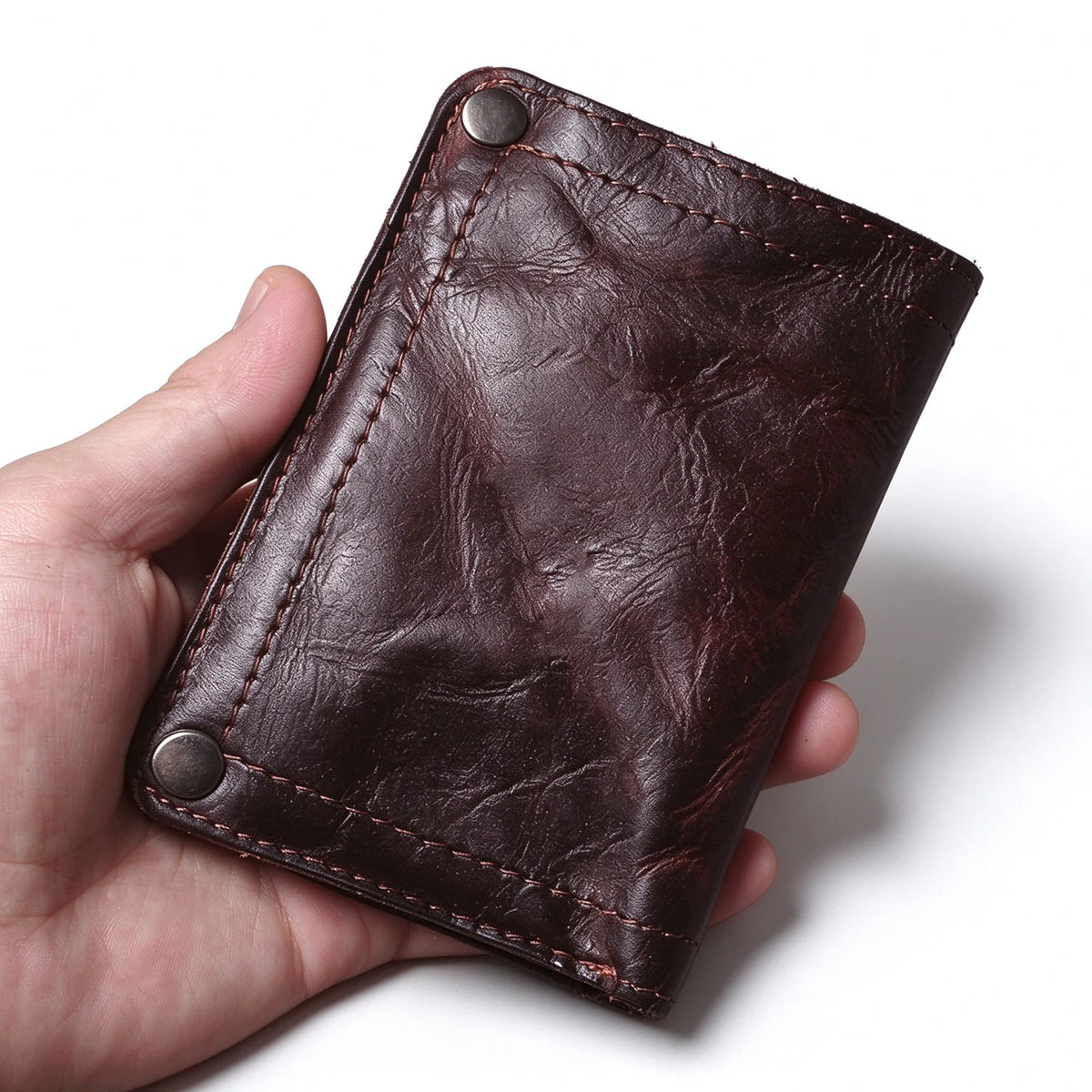 Dark brown leather bifold wallet held in one hand, showing the creased surface and two snap fasteners.