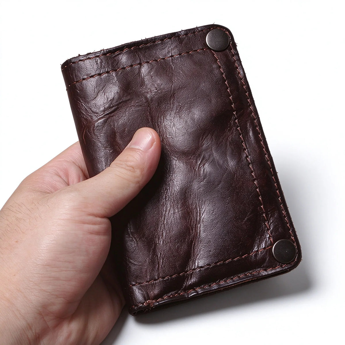 Front close-up of a hand-held dark brown leather wallet with stitched borders and corner snap fasteners.