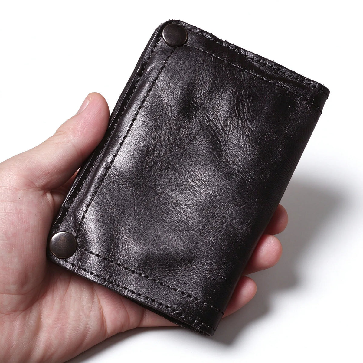 Black leather bifold wallet held in one hand, showing its textured front panel and two snap fasteners.